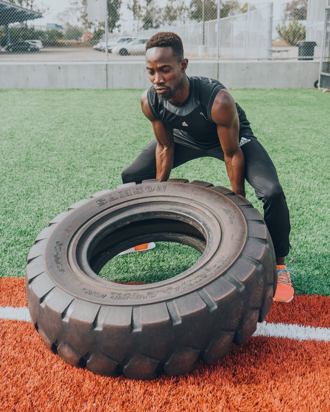 Yinka lifting a training tyre outdoors in black sportswear